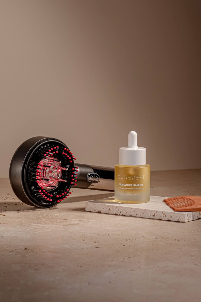 Styled product photography of Curerest Signature Hair Oil with hair brush and dryer, premium lifestyle composition for campaign use.