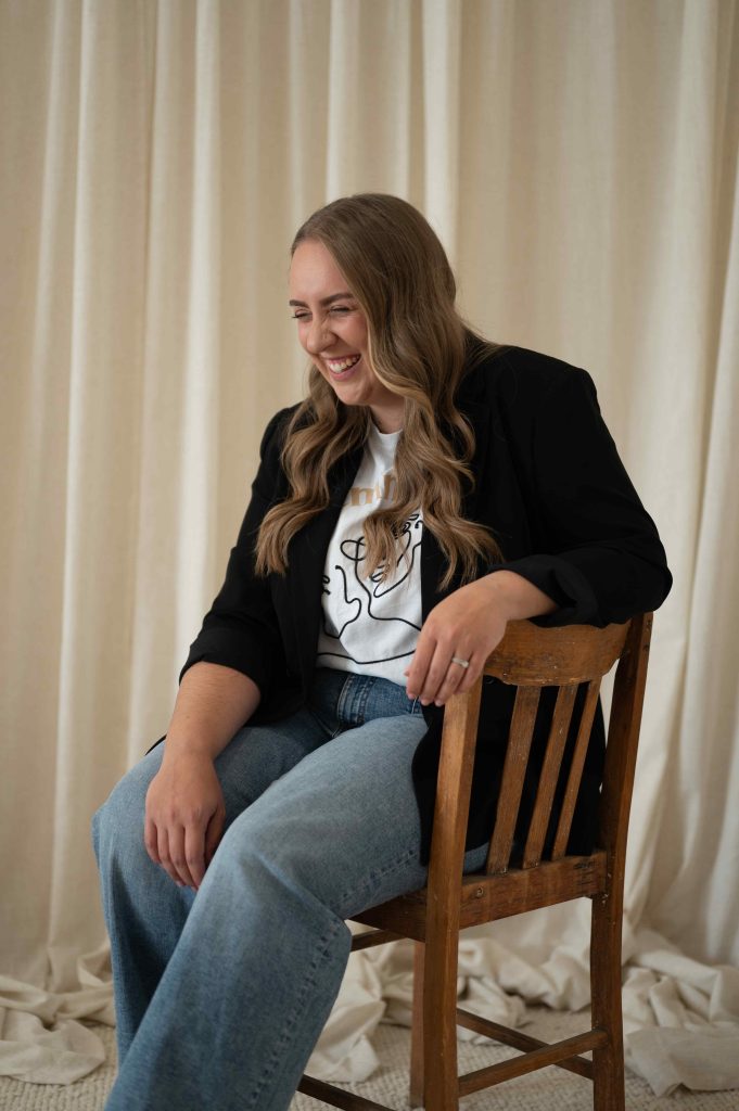 Woman in a black blazer laughing while seated on a wooden chair during a brand content session in Adelaide