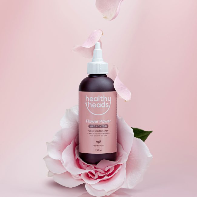 Bottle of Healthy Heads Flower Power treatment styled with pink rose petals against a soft pink background.