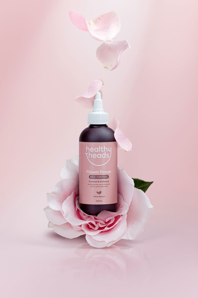 Bottle of Healthy Heads Flower Power treatment styled with pink rose petals against a soft pink background.