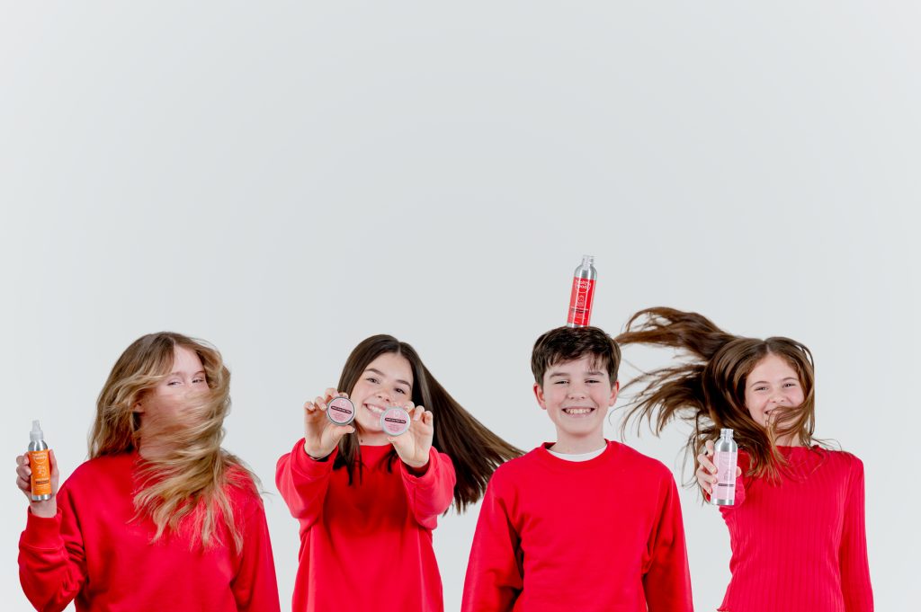 Children holding and balancing Healthy Heads haircare products while flipping their hair in a playful studio lifestyle product shoot.