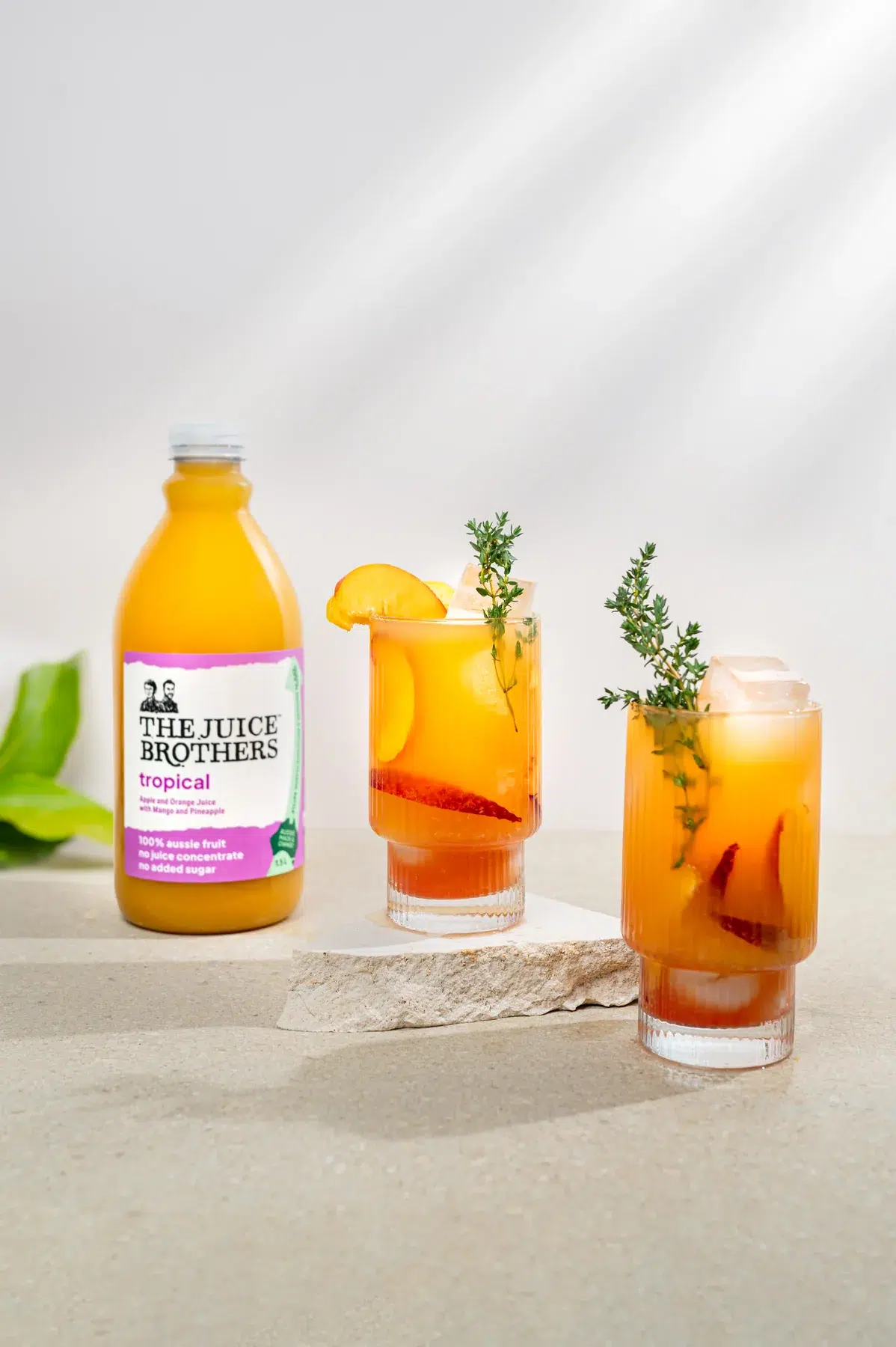 The Juice Brothers tropical juice bottle with two styled glasses garnished with peach and thyme