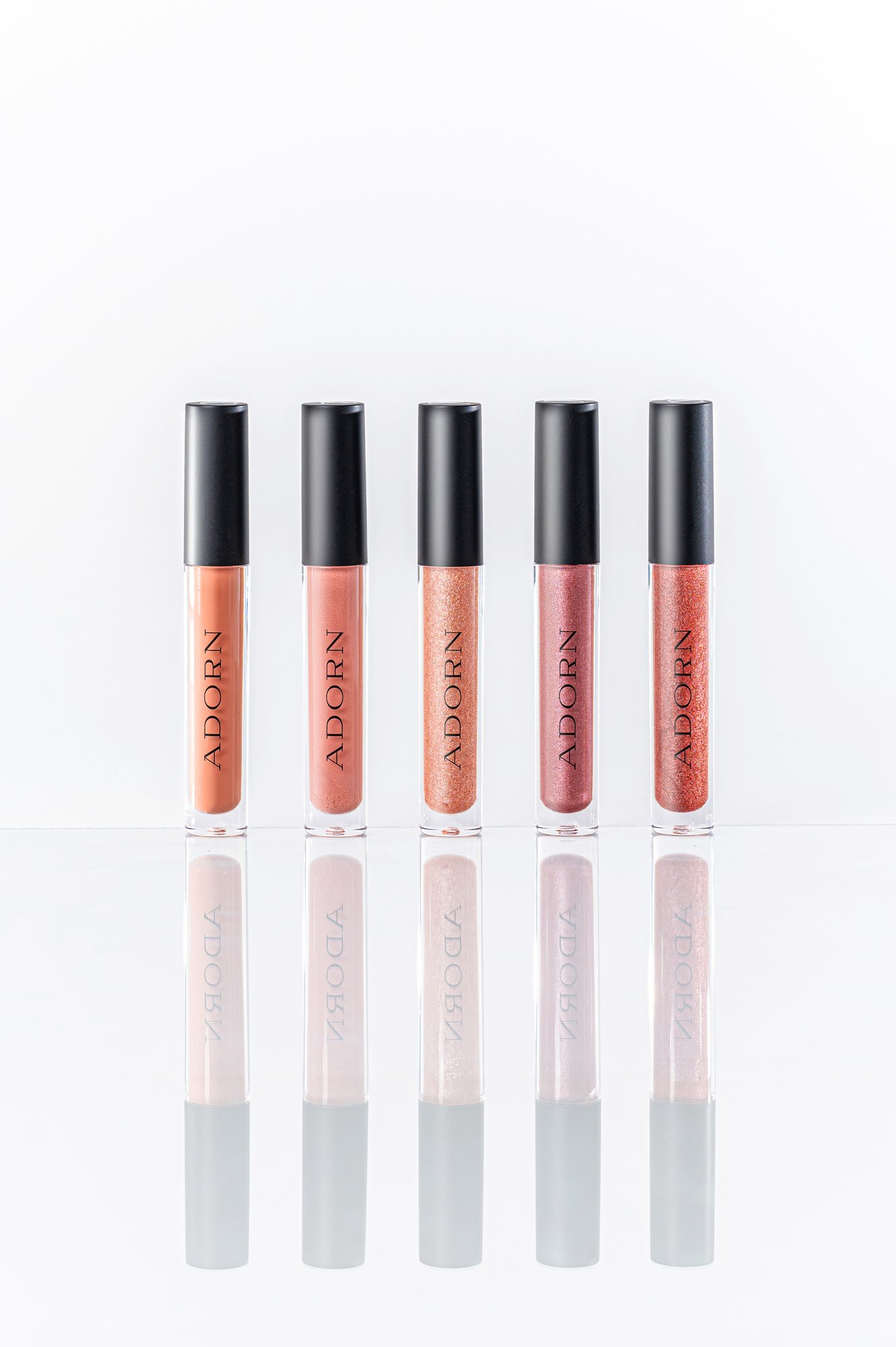 Five Adorn lip gloss shades standing in a row on a white reflective surface