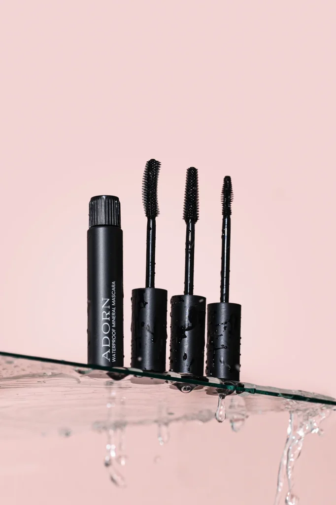 Adorn Waterproof Mineral Mascara tube and three wands on a wet glass edge with water dripping