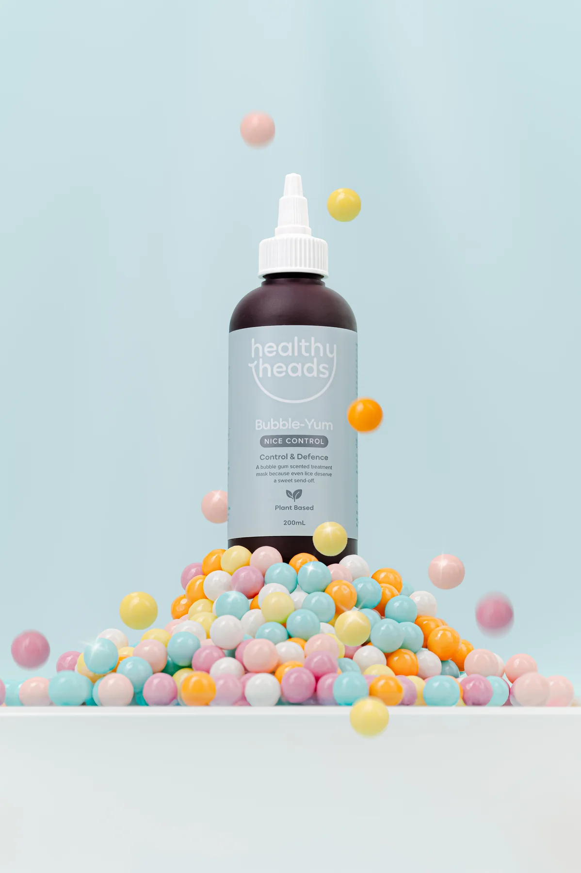 Healthy Heads Bubble-Yum treatment bottle on a pile of pastel gumballs against a blue background
