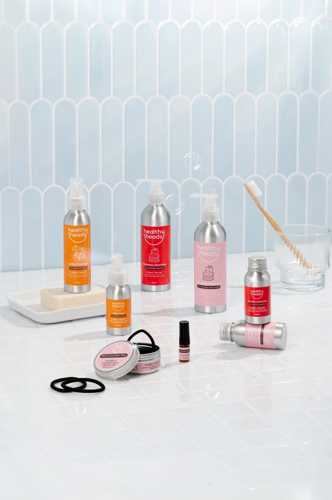 Healthy Heads range on a white tiled bathroom surface including Wild Orange spray, Strawberry Shortcake shampoo and conditioner, anti lice hair ties and an essential oil blend.