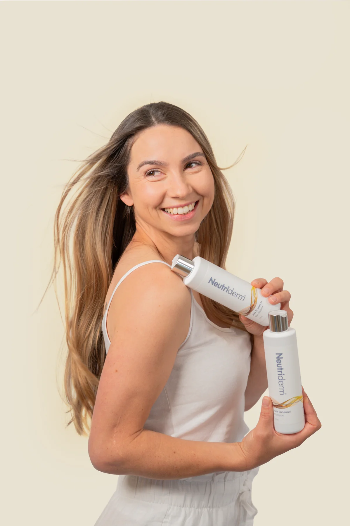 Smiling woman holding Neutriderm Hair Enhancer shampoo and conditioner against a neutral background