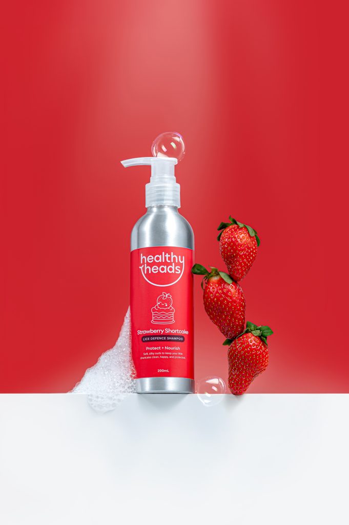 Healthy Heads Strawberry Shortcake lice defence shampoo with fresh strawberries on a bold red background