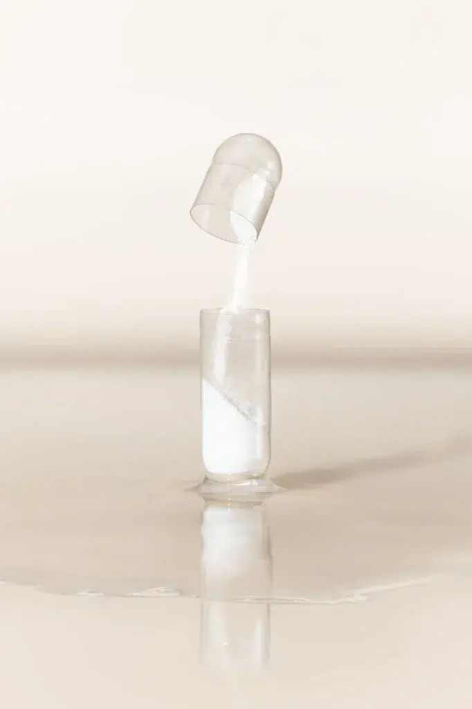White magnesium powder pouring between two clear vessels with a reflection on a cream surface
