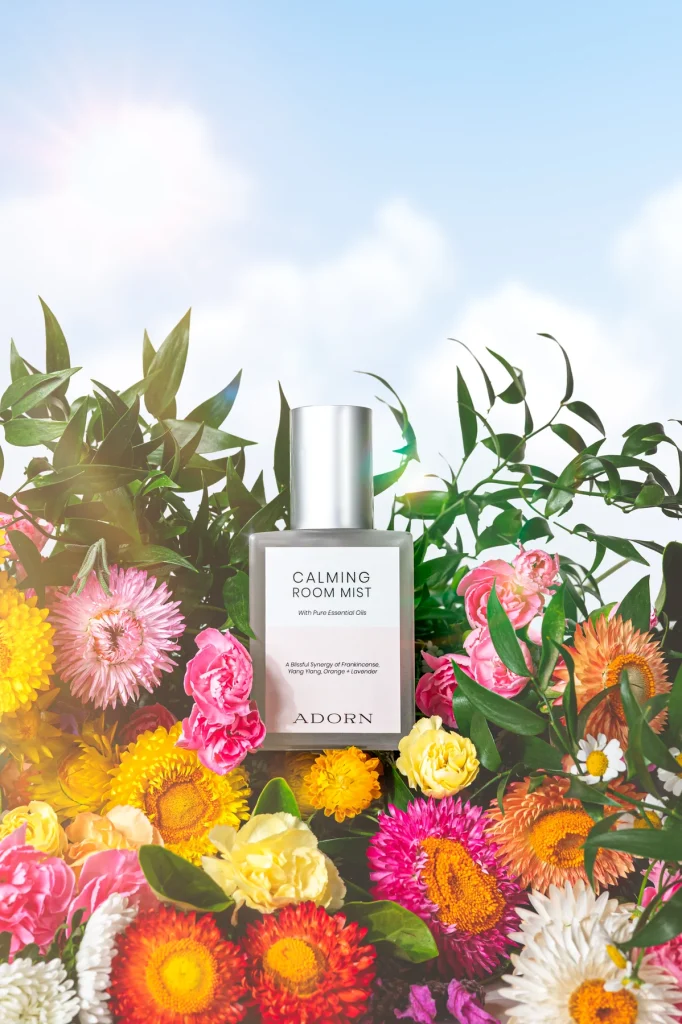 Adorn Calming Room Mist bottle surrounded by colourful everlasting flowers under a soft blue sky