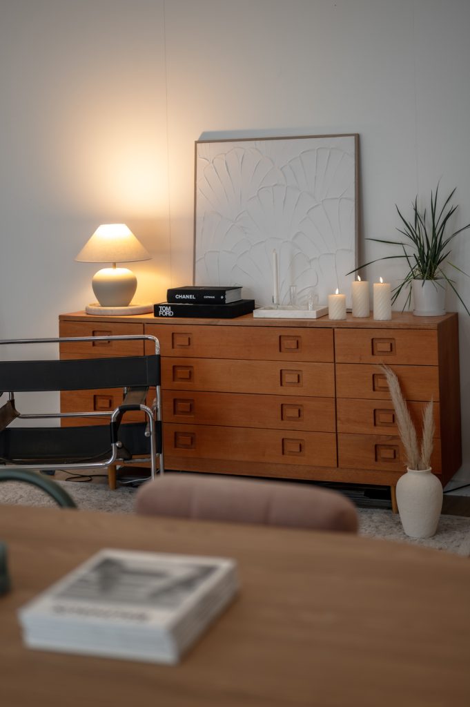 Timber sideboard styled with a lamp, books, candles, artwork and plants inside the studio