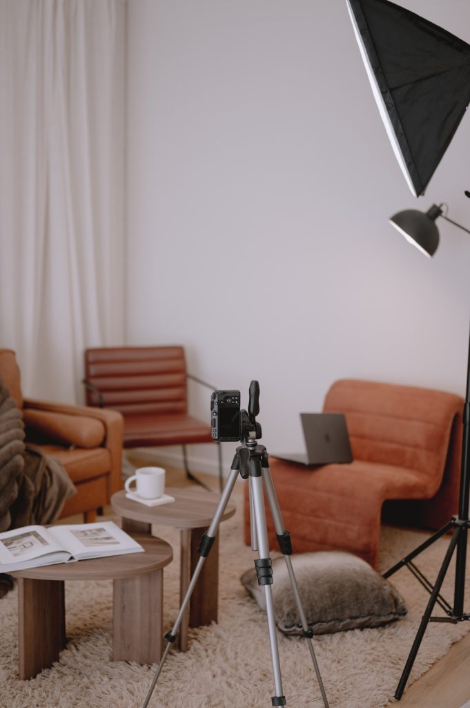 Camera on a tripod with studio lighting positioned in front of a styled lounge set